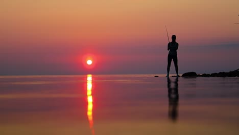 Frau-Fischt-Auf-Angelrute,-Die-Sich-Bei-Sonnenuntergang-Im-Hintergrund-Dreht.