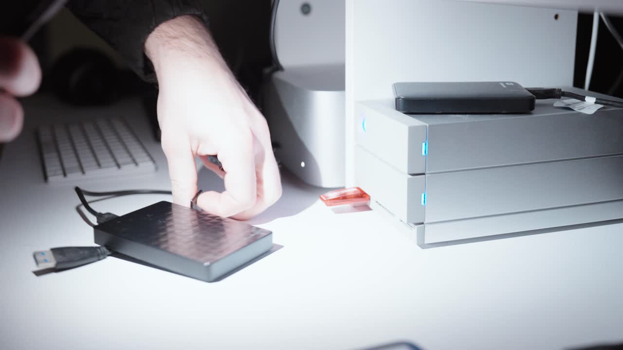Nærbillede af en person, der tager eksterne drev og USB-enheder ved siden af en desktopserver med glødende indikatorlamper, der illustrerer datatyveri, cybersikkerhedsrisici og uautoriseret adgang.