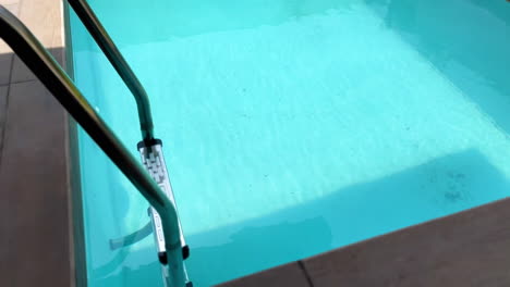 crystal clear turquoise blue water in a swimming pool with ladder, slow moving high angle shot