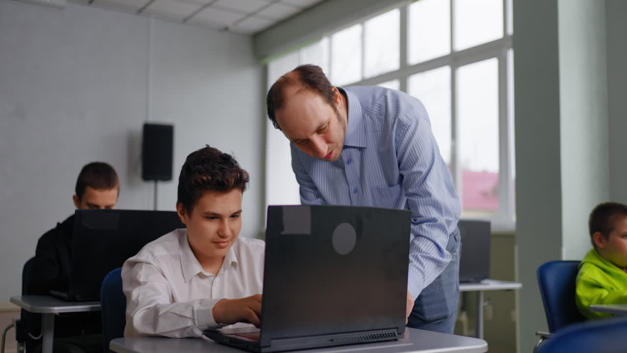 maestro ayudando a un estudiante con una computadora portátil en un aula