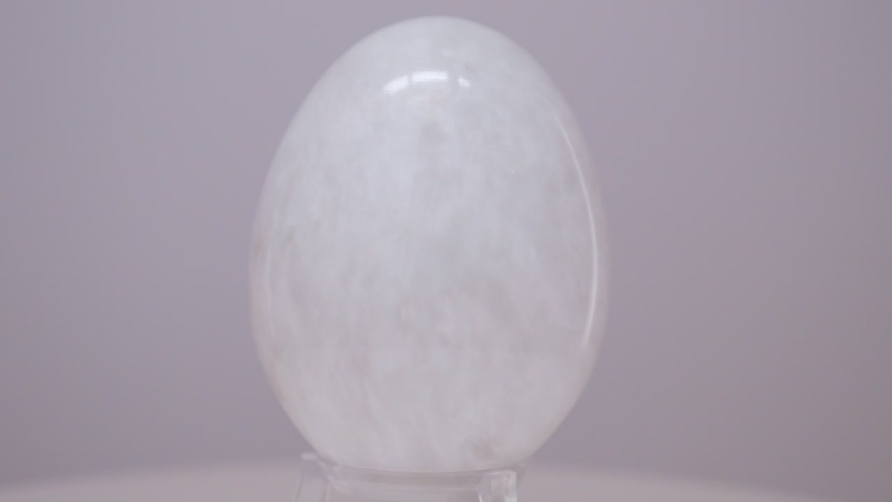 Uovo di marmo bianco che ruota lentamente su un piatto girevole davanti a uno sfondo bianco.