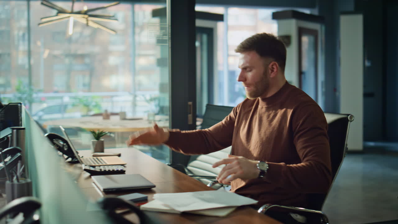 CEO nervoso finisce videoconferenza tenendo i documenti alla scrivania del portatile in ufficio
