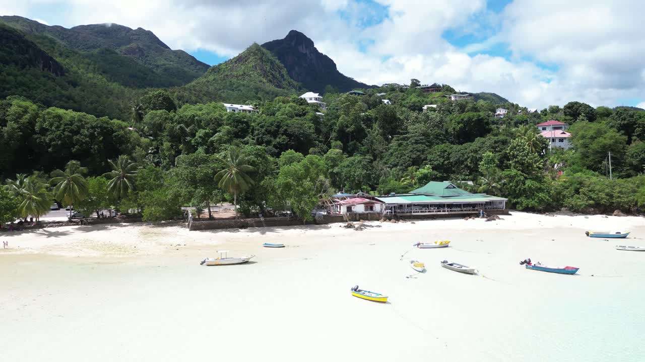Bright sunlight on white sand empty beach island of Mahe with fishing boats at shore, Indian Ocean, Drone shot