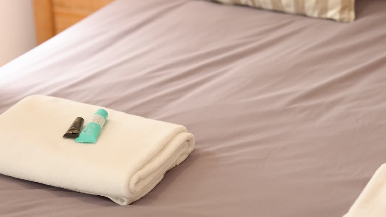 Hands arranging towels and toiletries on a neatly made bed in a softly lit hotel room