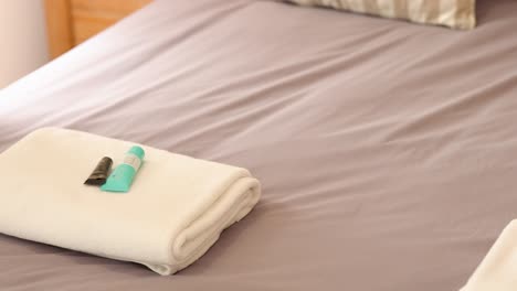 hands arranging towels and toiletries on a neatly made bed in a softly lit hotel room
