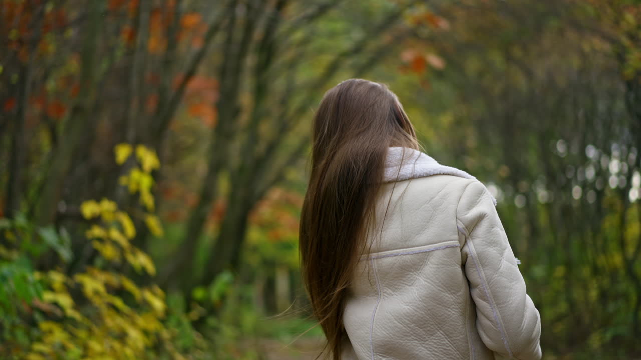 Caucasian lady walking in the nature turns around waving her beautiful long hair. Blurred natural autumn backdrop.