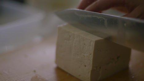 organic vegan soy tofu being sliced with kitchen knife