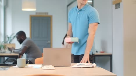 hombre guapo poniendo regalo en la mesa de un colega en el coworking.