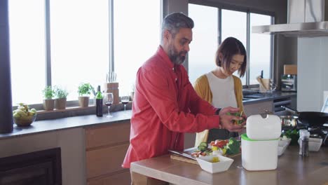 Happy-diverse-couple-cooking-together,-chopping-vegetables-and-cleaning-in-kitchen