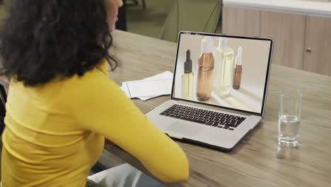 mujer biracial en la mesa usando portátil, compras en línea de productos de belleza, cámara lenta