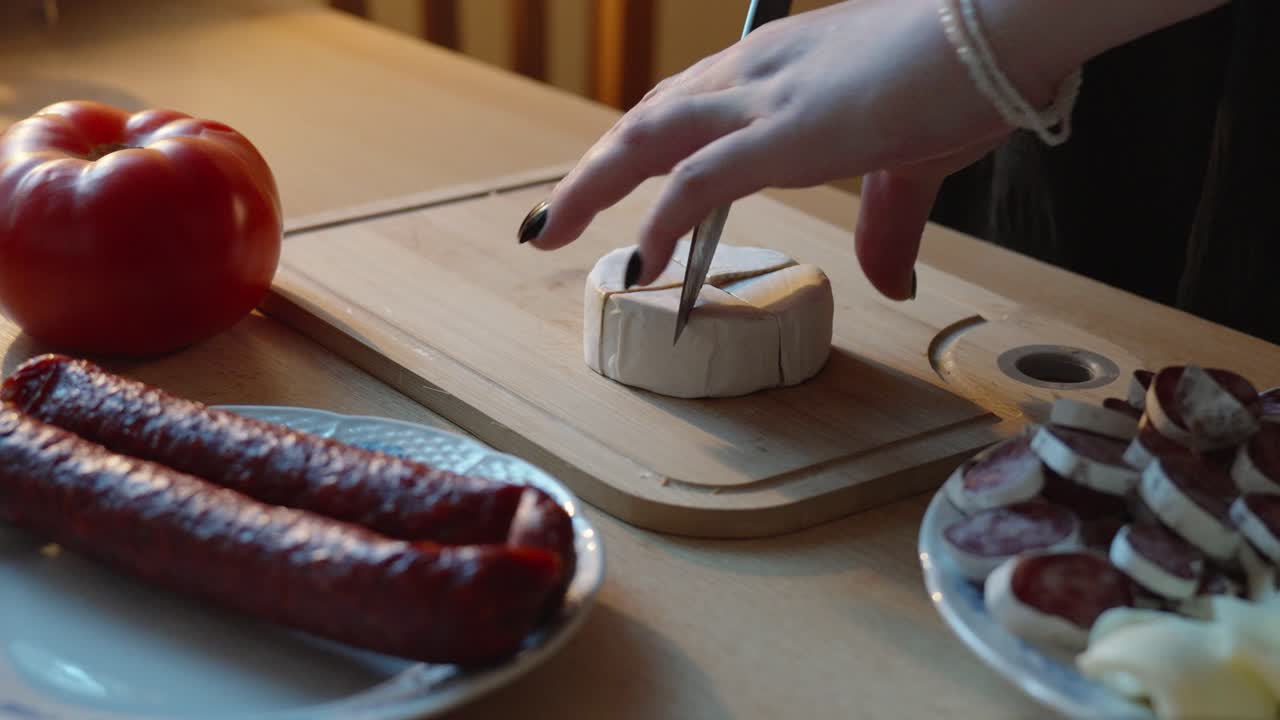 Girl slicing camembert cheese in the kitchen. Preparing evening snacks with salami and sausages