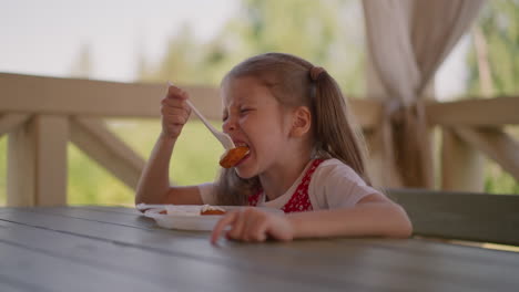 grimacing little girl bites hot curd fritter in street cafe