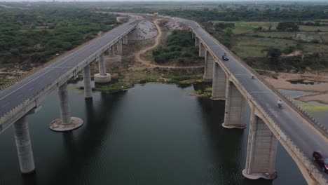 highway bridge built over the river basin in the indian rural terrain, slow motion drone shot