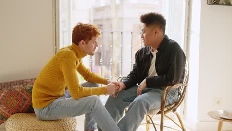 diverse male couple holding hands and talking at home