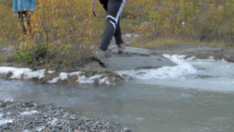 a woman in boots running and jumping across an icy stream in norway, slow motion