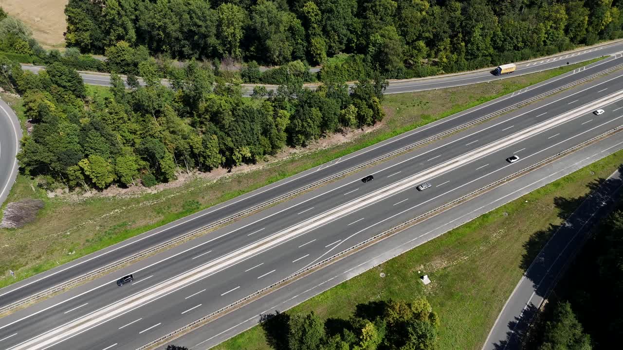 Traffic on highway with trucks on exit near green forest trees and farm fields. Sunny Day in summer. Suburb of town in midwest of america. Aerial top down flyover