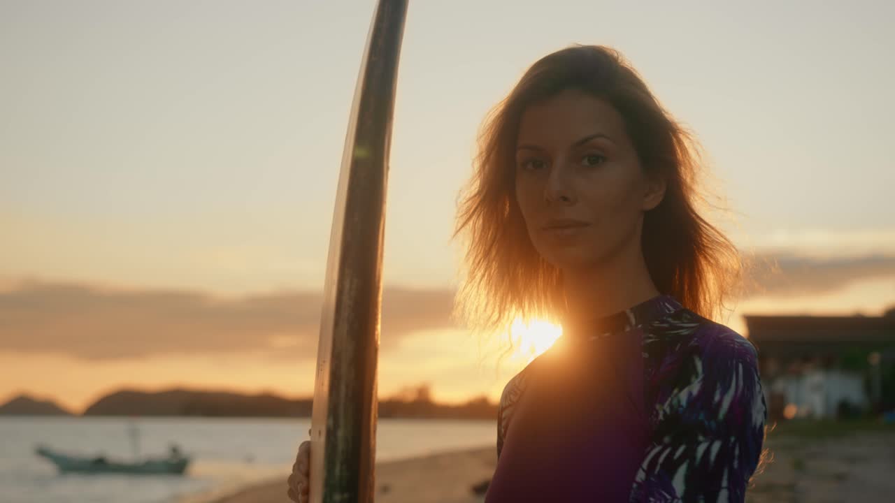 Donna con tavola da surf sulla spiaggia al tramonto