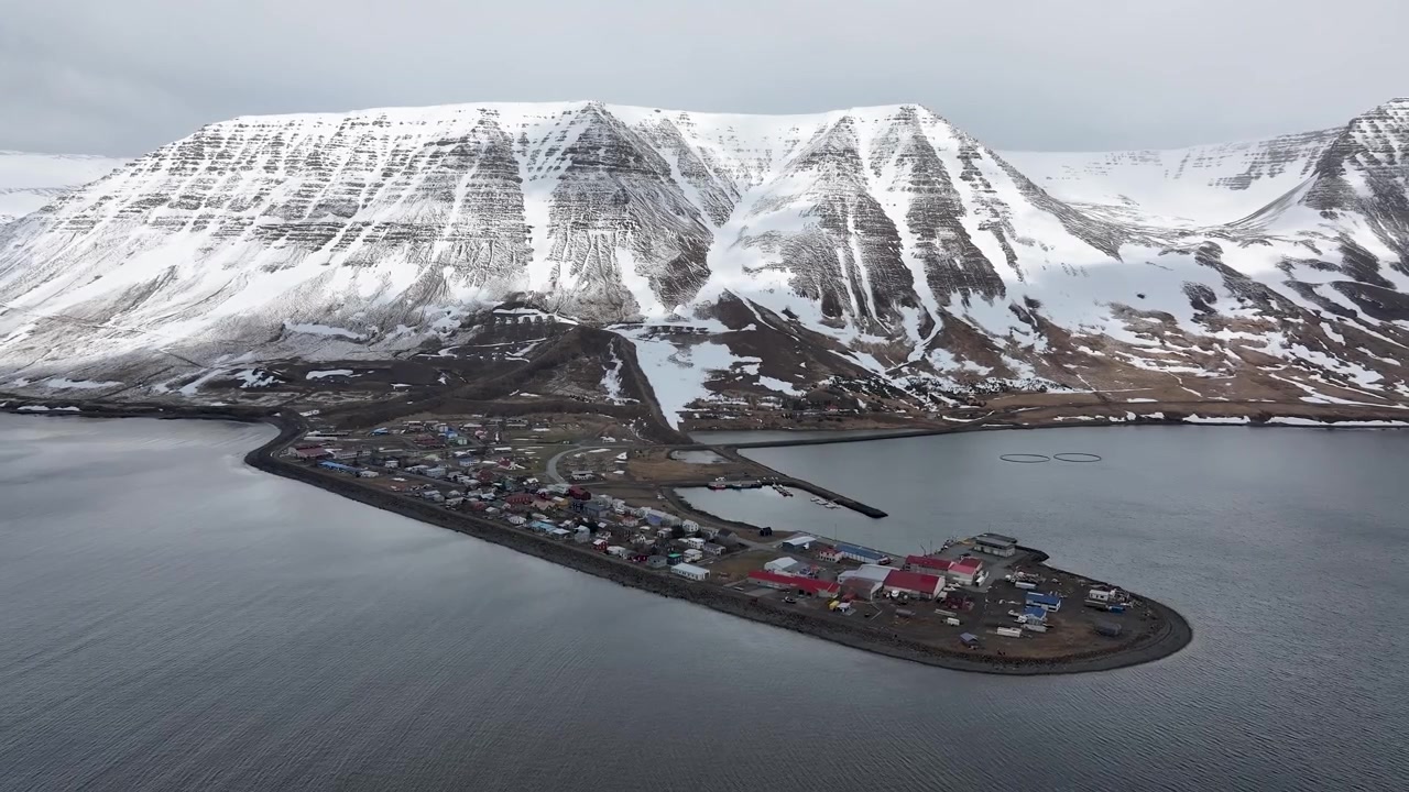 Droneopptak fanger Flateyri landsbyhalvøy som ligger i et snødekt fjordlandskap omgitt av dramatiske islandske fjell om vinteren.