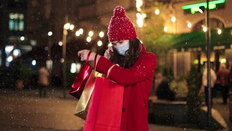 retrato de una joven feliz y hermosa hablando por teléfono inteligente y sosteniendo bolsas de compras en la calle mientras nieva en navidad