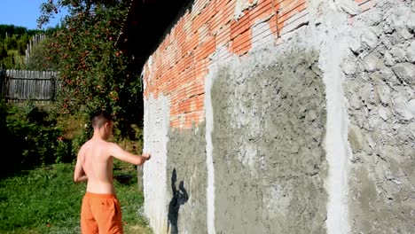 young man works on a stucco cement wall on a building that's under construction