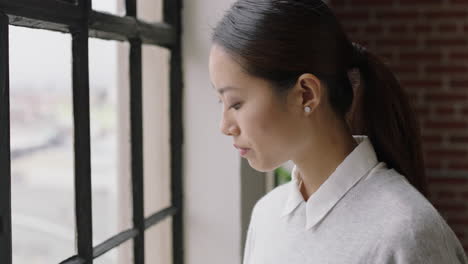 beautiful asian business woman drinking coffee at home using smartphone enjoying relaxed morning browsing messages looking out window planning ahead texting on mobile phone networking