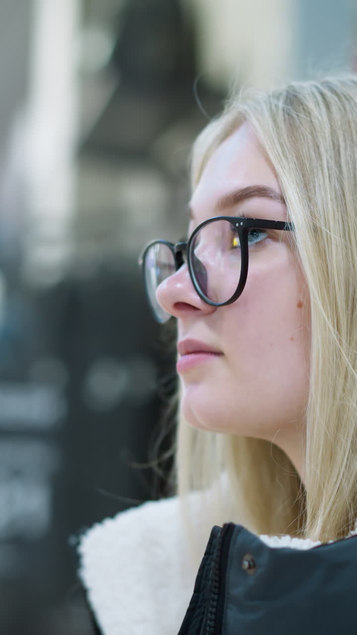 vista lateral de primer plano de una estudiante con capucha negra caminando en un centro comercial bien iluminado, se ve tranquila mientras el fondo borroso presenta un espacio comercial con personas que pasan, creando una atmósfera de compras relajadas