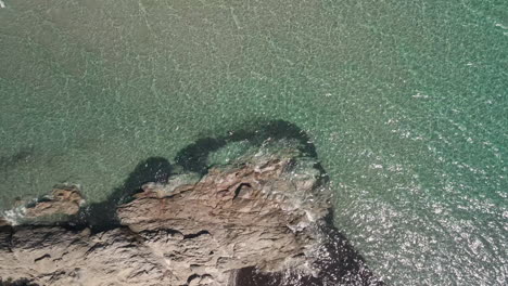 Top-View-Of-Rocky-Coastline-With-Splashing-Waves-From-Crystal-Blue-Sea-Of-Sardinia,-Italy-During-Summer