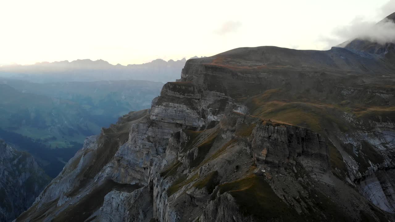 una vista aérea giratoria del punto de vista de muttenchopf del lago limmernsee en glarus, suiza, con los alpes suizos, acantilados, agua azul, excursionistas a la vista después de una puesta de sol