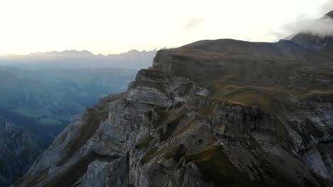 A-spinning-aerial-view-of-Muttenchopf-viewpoint-of-lake-Limmernsee-in-Glarus,-Switzerland,-with-the-Swiss-Alps,-cliffs,-blue-water,-hikers-in-view-after-a-sunset