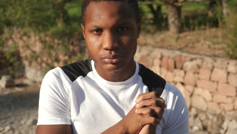 portrait of young black man warming up wrists before running outdoors looking at camera