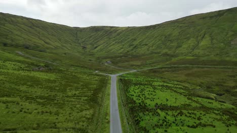 Drone-shot-of-a-car-driving-towards-Glenniff-Horseshoe,-flying-forwards-along-the-road-with-farmland-all-around