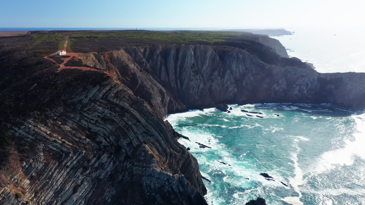 Agitated Ocean water crashing against high cliff wall during sunlight