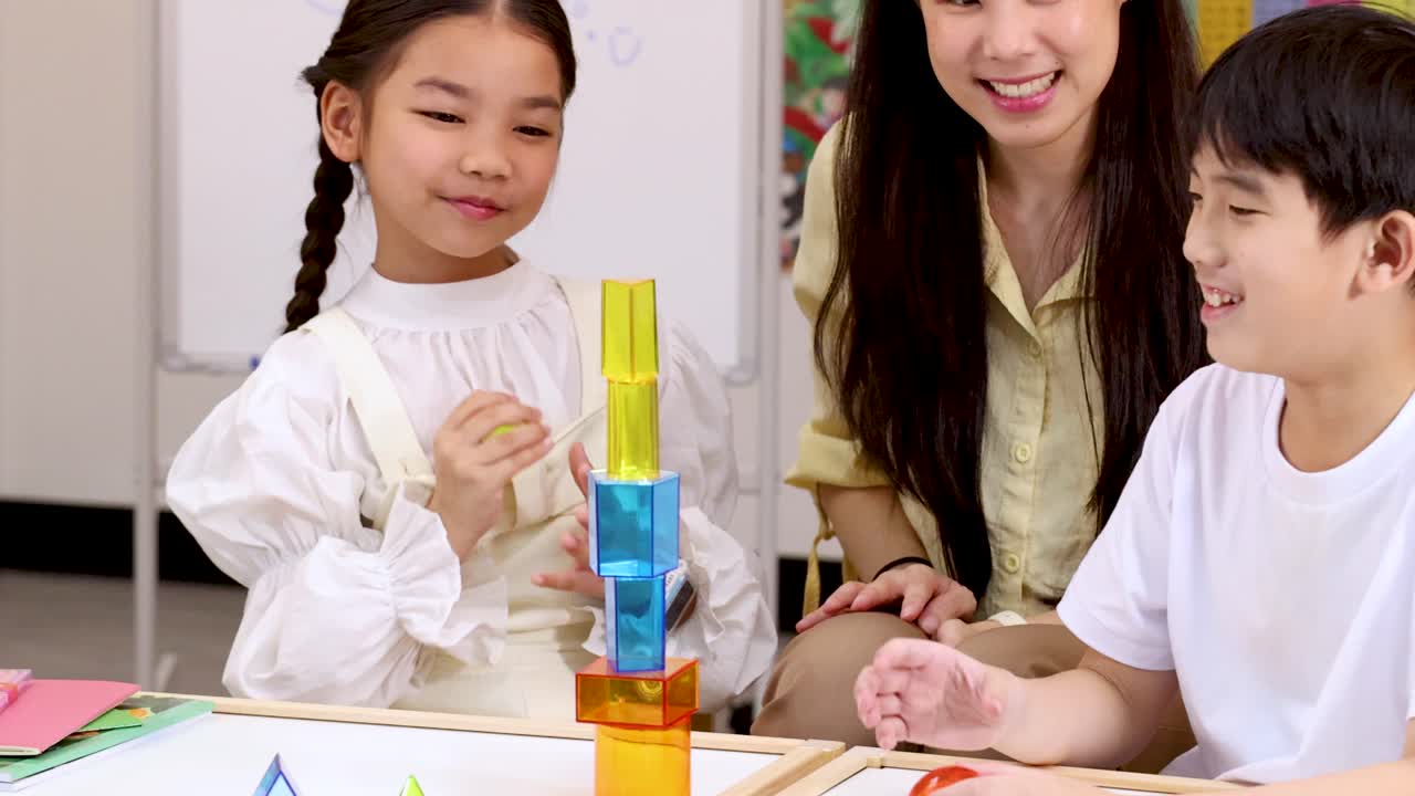明るい教室で、子供2人と先生が交流し、カラフルなブロックを積み重ねている。楽しく創造的な雰囲気