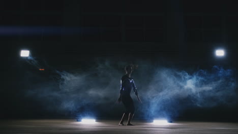 una talentosa gimnasta realiza un giro en un salto en la alfombra de gimnasia en cámara lenta en una luz contorneada en el humo. steadycam. la rotación en el aire. acrobacias.