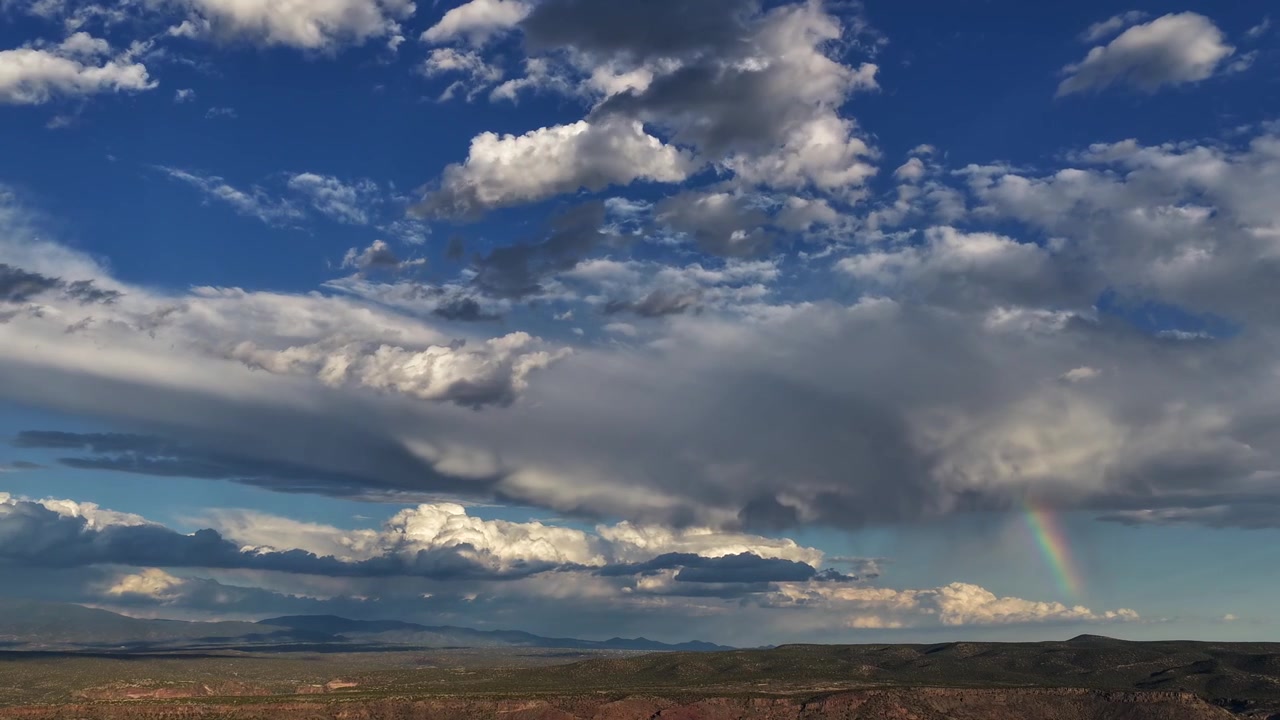 Timelapse 4K con drone che cattura un clima regionale mutevole e condizioni meteorologiche dinamiche. Un segmento vibrante di arcobaleno risplende sotto nuvole temporalesche mozzafiato sopra una cresta scura nella regione dei quattro stati