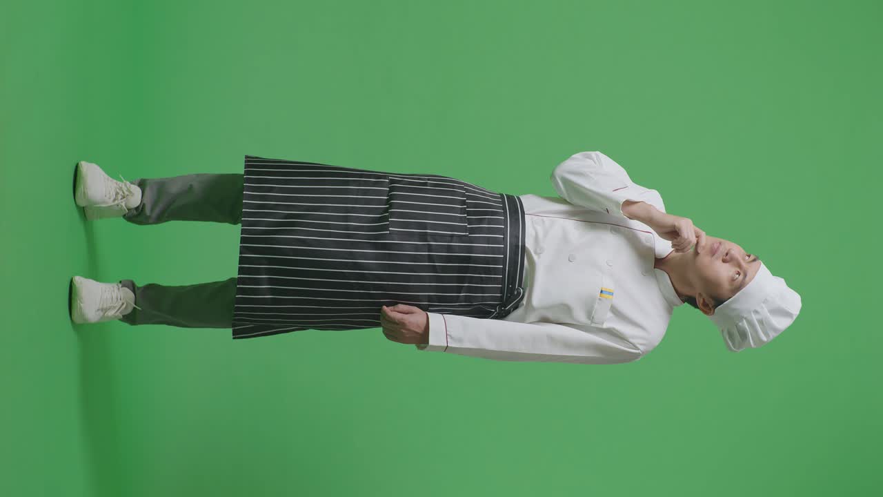 아시안 남성의 몸이 가득 차있는 요리사는 생각하고 주위를 둘러보고 녹색 스크린 배경 스튜디오에 서있는 동안 지표손가락을 들어 올립니다.