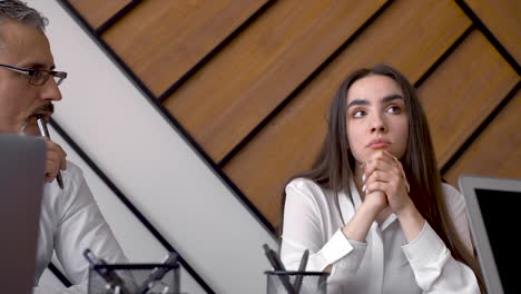 concerned young brunette woman talking with co workers and hiding her face behind her hands