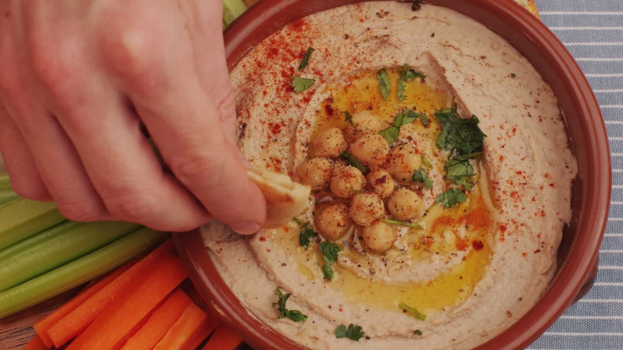 Hummus among fresh vegetables on table top view. Hummus garnished with chickpeas, olive oil, spices and greens. Hummus or fava, a hearty snack of legumes. Kosher healthy vegan food. Lean, vegetarian dish