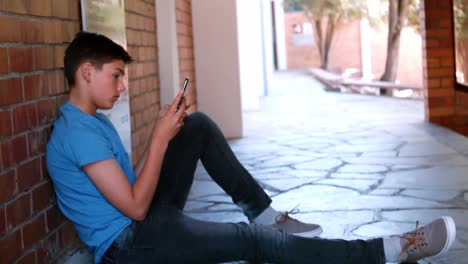 Schoolboy-sitting-in-corridor-and-using-mobile-phone