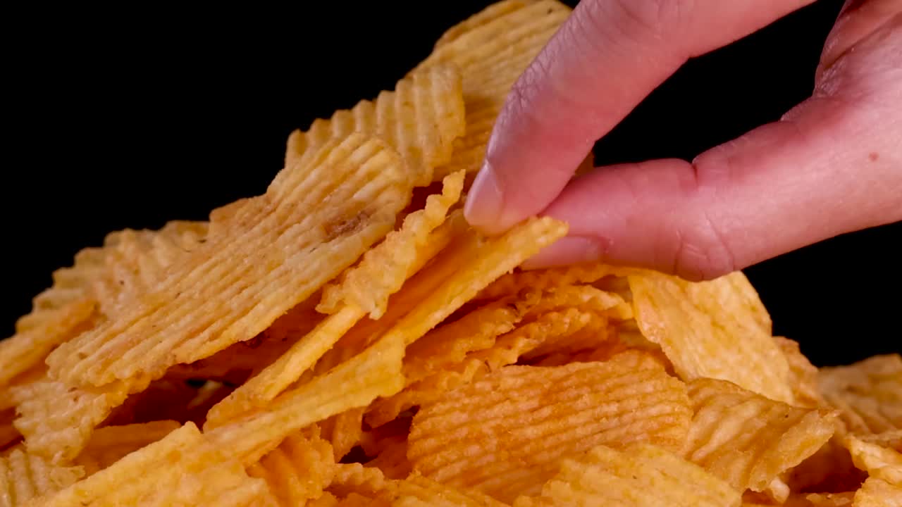 Un primo piano di dita che selezionano una singola patatina ondulata da un mucchio dorato
