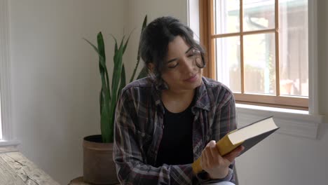 Joyful-Puerto-Rican-girl-smiling-enjoying-finishing-book-story-looking-at-cover-in-appreciation