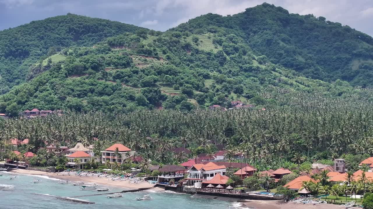 Tropical Island vibe of Balinese Candidasa Beach with hotel by palm tree plantation. Aerial drone