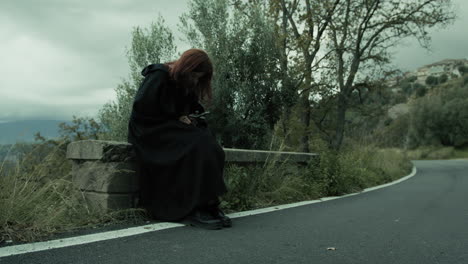 christian woman prays with crucifix sitting beside a road in nature