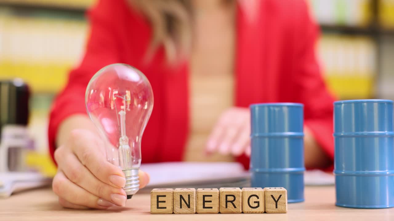 Cubi di legno formano la parola energia vicino a barili di petrolio giocattolo su una scrivania da ufficio.