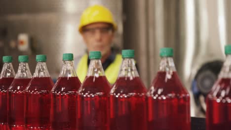 Worker-checking-juice-bottles-on-production-line