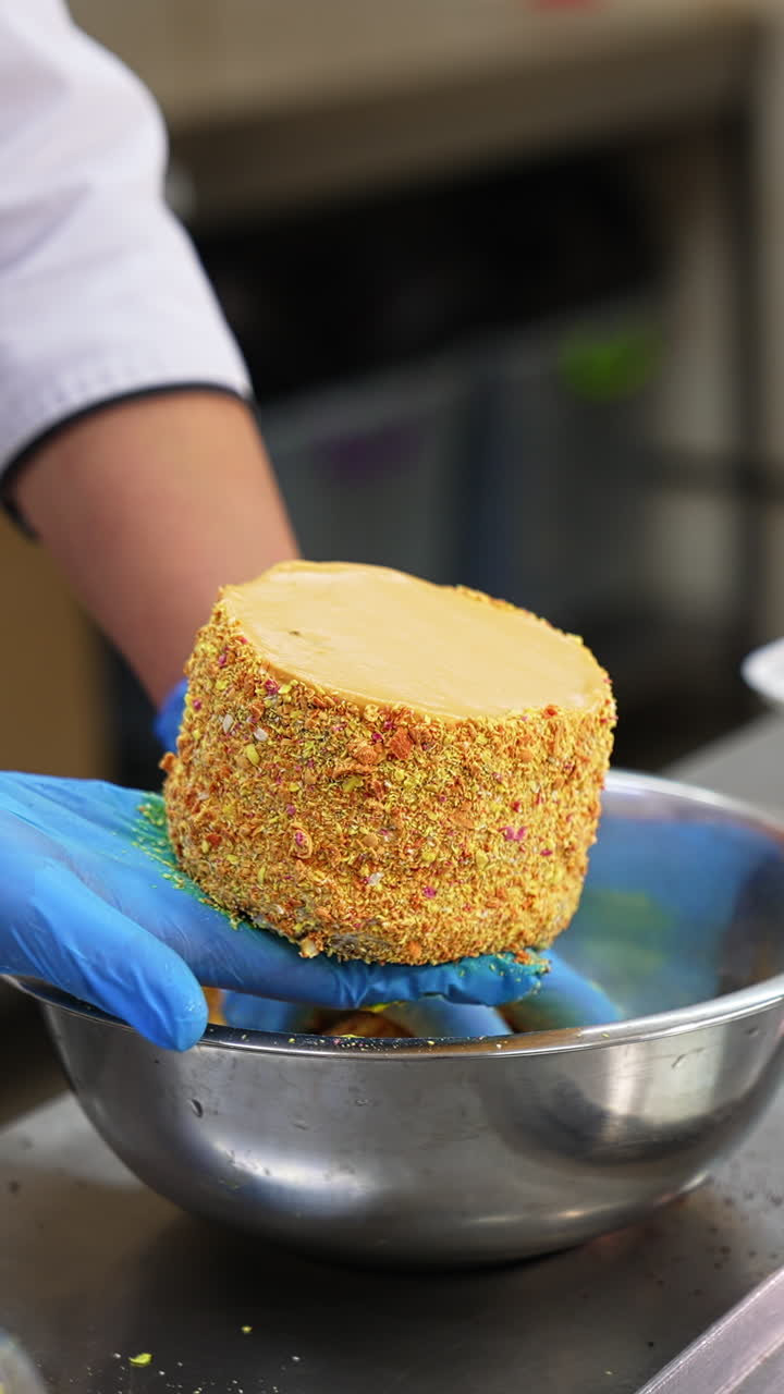 Food factory worker covers the cakes with yellow sprinkling. Close up. Ready-made desserts being put in separate boxes. Blurred backdrop. Vertical video
