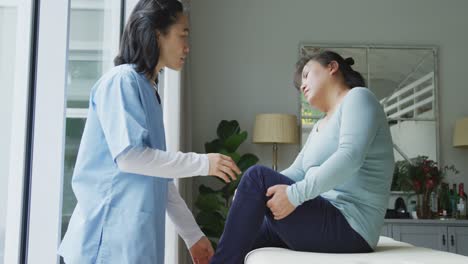 asian female physiotherapist treating female patient holding knee in pain at surgery