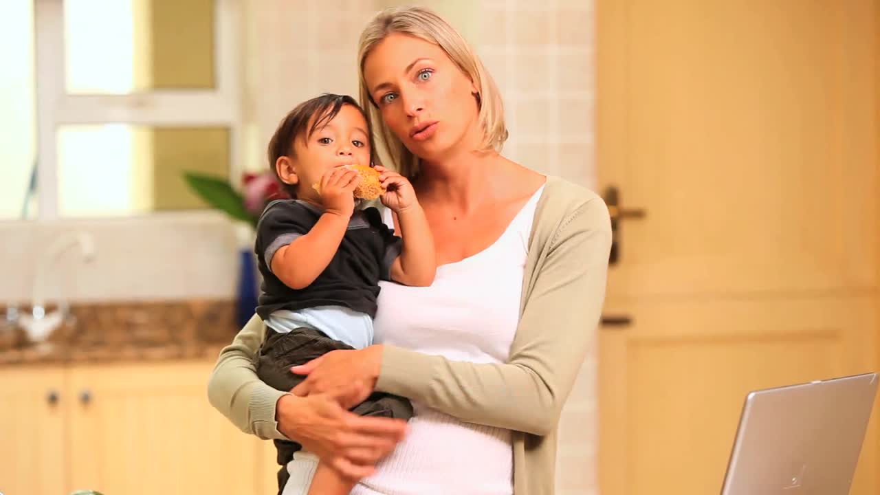 부에서 피곤한 어머니가 아기를 들고 노트북으로 일하고 있습니다.