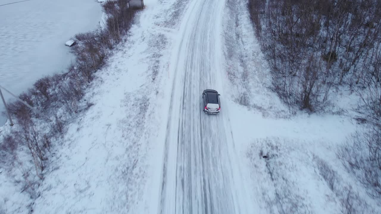 Car travelling through frozen snowy forest road - Overhead Aerial tracking shot