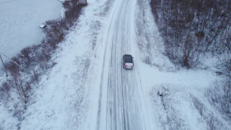 car travelling through frozen snowy forest road - overhead aerial tracking shot